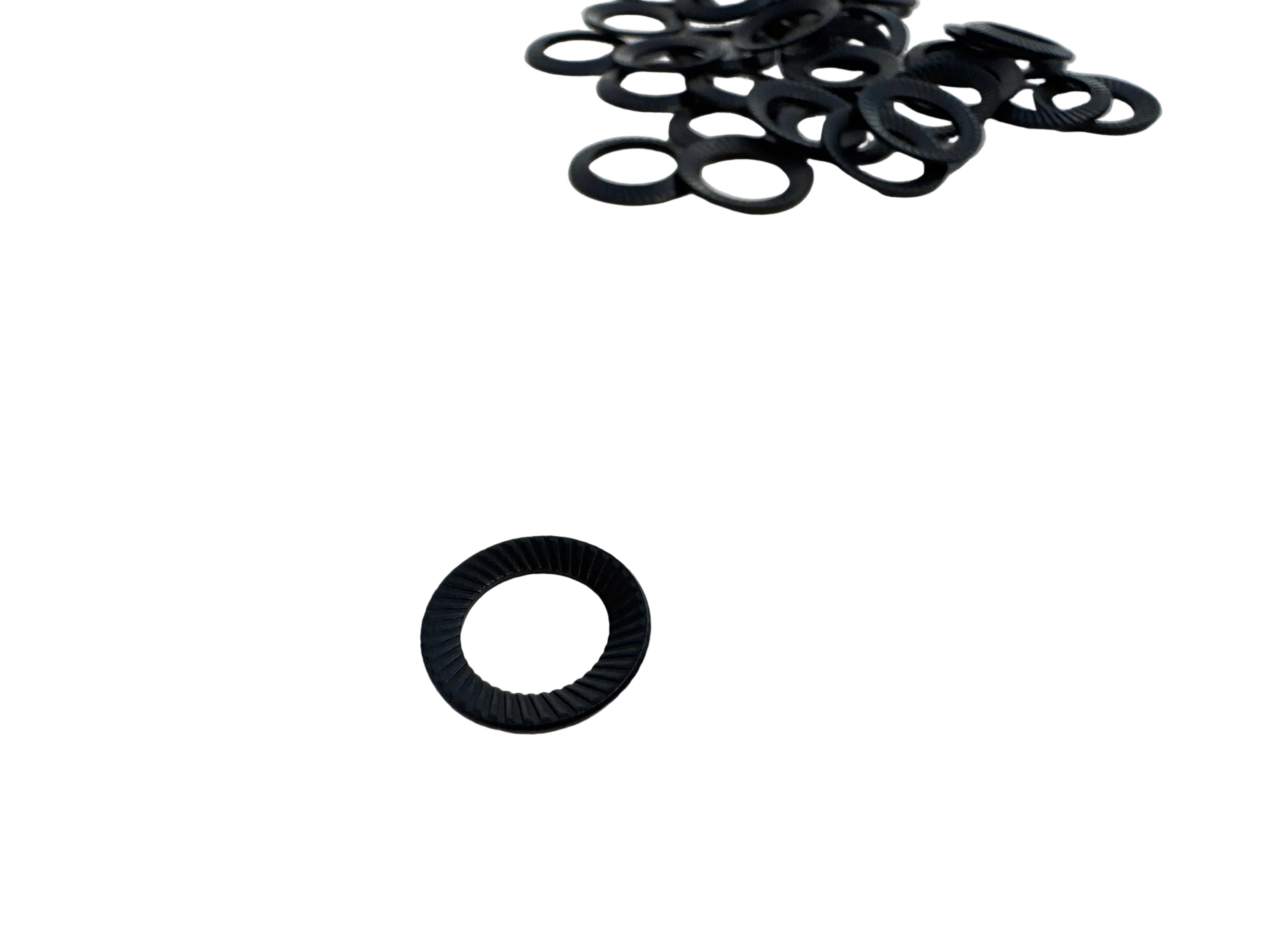 A small black circular ring-shaped component with a threaded inner edge, shown on a light gray surface with several similar rings piled in the upper right.