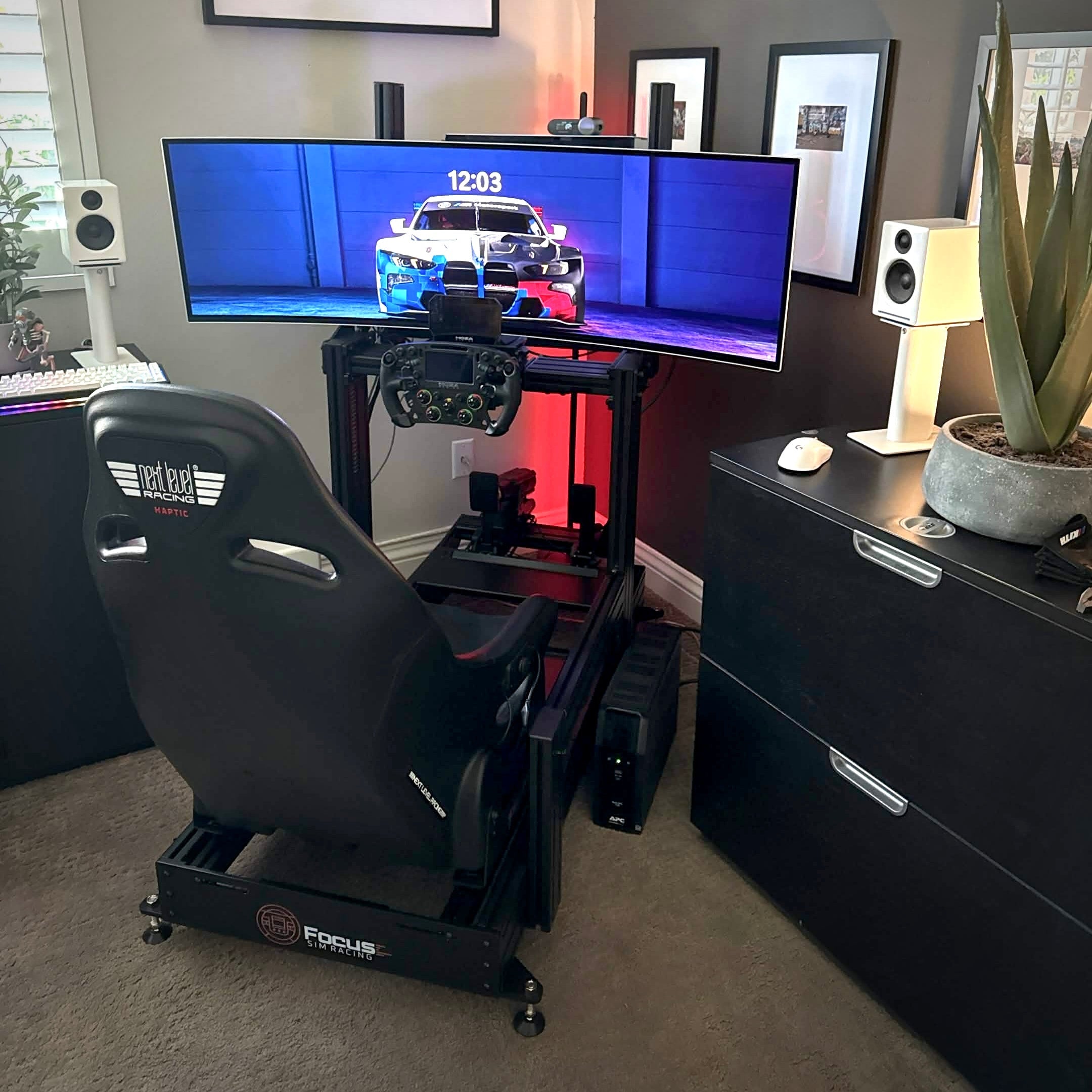 Gaming setup with a racing chair, multiple monitors, and gaming accessories in a room.