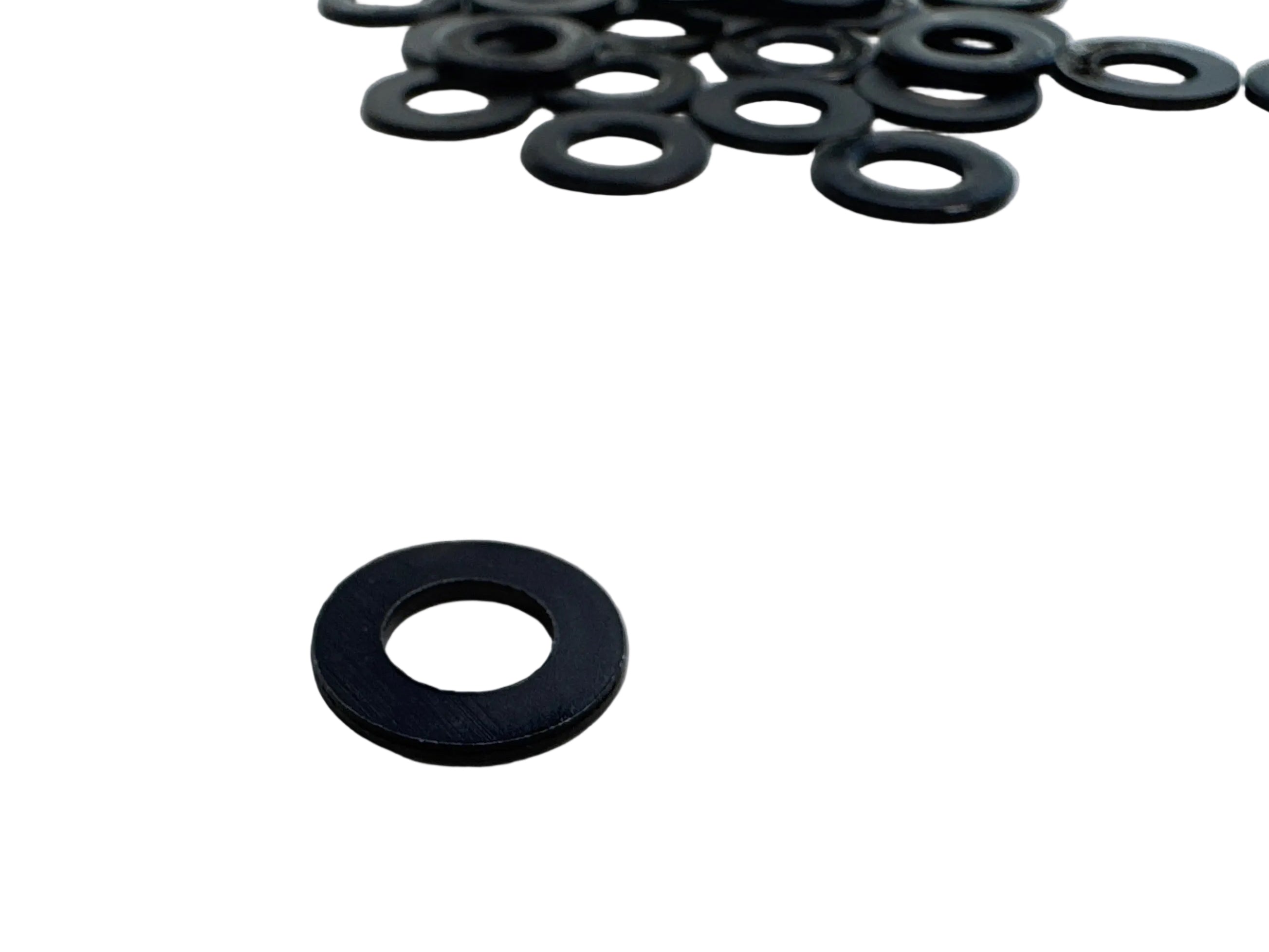Black rubber O-rings or washers, with one placed prominently in the foreground and several more scattered in the upper right on a light gray surface.